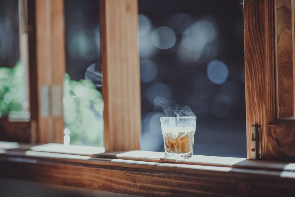 A steaming hot drink in a glass catching sunlight on a wooden window sill, evoking warmth and relaxation.